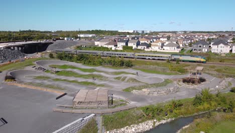 aerial of bmx bike park on sunny day in suburbia as 2 teens ride, a train goes by
