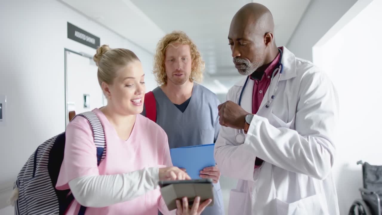 Diverse doctors discussing work and using tablet in corridor at hospital, slow motion