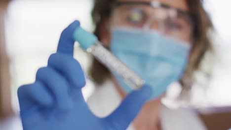 Female-teacher-wearing-face-mask-and-protective-glasses-holding-a-test-tube-in-laboratory