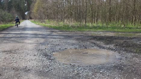 niño en edad preescolar despreocupado en paseos en bicicleta en charco en el bosque de primavera