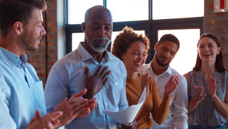 colleagues clapping and shaking hands with businessman leading team meeting in multi-cultural office