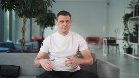 young handsome man speaks, looking into the camera and gesturing with his hands against the backdrop of a stylish office