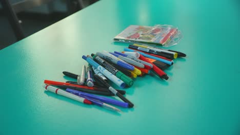 pens, pencils and markers of divers colors on a green table lens whack focus rack close up