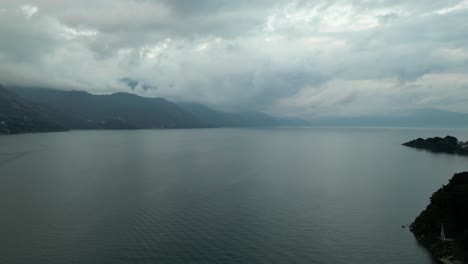 Drohnenansicht-In-Guatemala,-Die-An-Einem-Bewölkten-Tag-In-Atitlan-Einen-Blauen-See-Schwenkt,-Der-Von-Grünen-Bergen-Und-Vulkanen-Umgeben-Ist