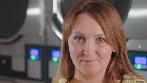 Portrait view of house wife in yellow shirt inside modern laundromat, soft blur of washer drums behind, calm face with blue eyes, subtle smile, clean service vibe, hygiene focused setting
