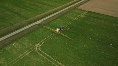 Tractor-Con-Pulverizador-Arrastrado-Sigue-Las-Pistas-En-Un-Campo-Y-Gira-A-La-Derecha,-Vista-Aérea