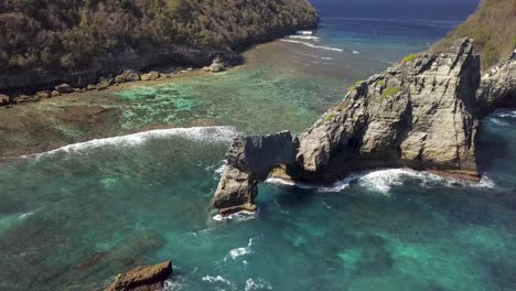 aerial view of atuh beach on nusa penida, indonesia on a sunny day and with crystal blue water hitting the rock formations