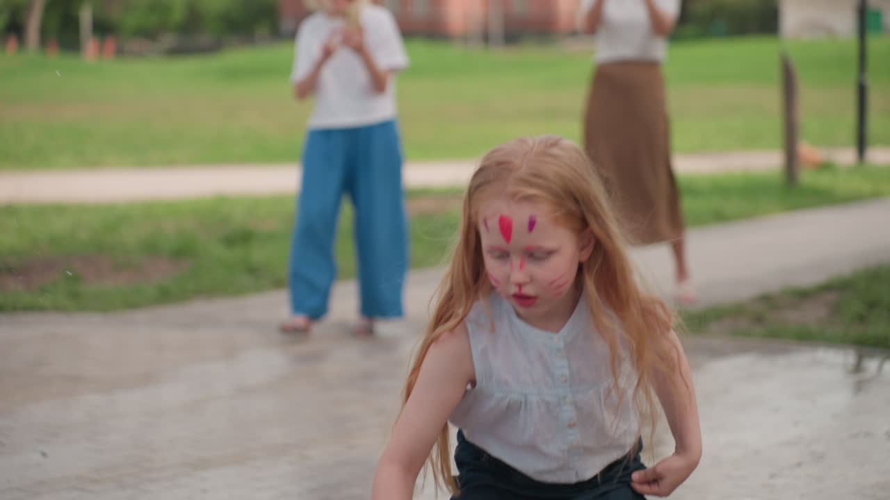 Face painted kids pointing and admiring waterfall in outdoor park, blurred parents holding camera in background, joyful surprise and shared family moment on sunny day