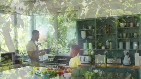 animation of leaves over happy african american father and son cooking together