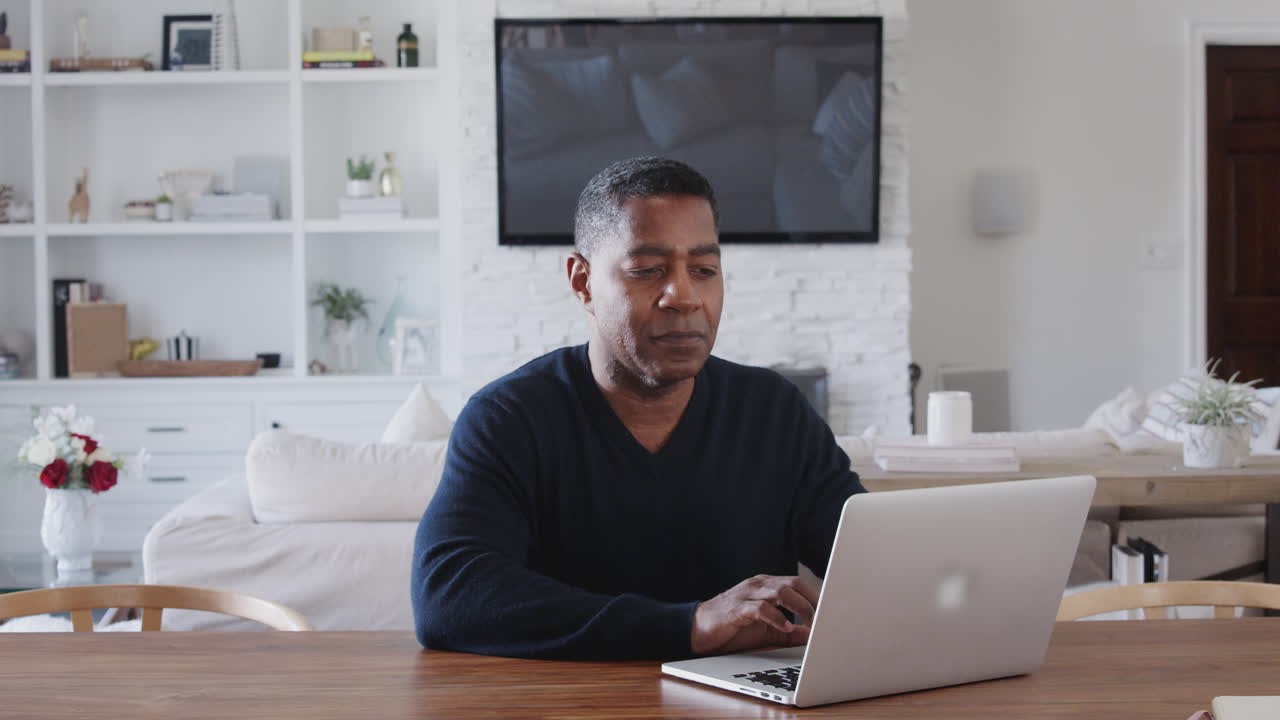 Middle aged African American man sitting at a table using laptop computer at home, close up, zoom in
