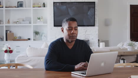 Middle-aged-African-American-man-sitting-at-a-table-using-laptop-computer-at-home,-close-up,-zoom-in