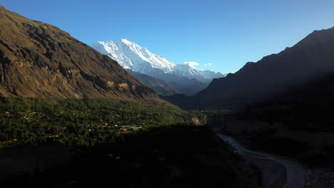 Cinematic-drone-shot-of-the-sun-shining-in-the-valley,-Passu-Cones-in-Hunza-Pakistan,-snow-covered-mountain-peaks-with-steep-cliffs,-high-rotating-aerial-shot