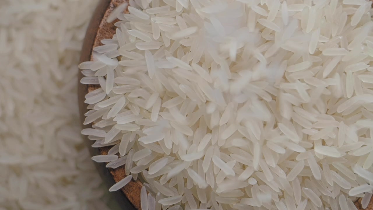 Raw Rice Grains Falling into a Wooden Bowl, Top View