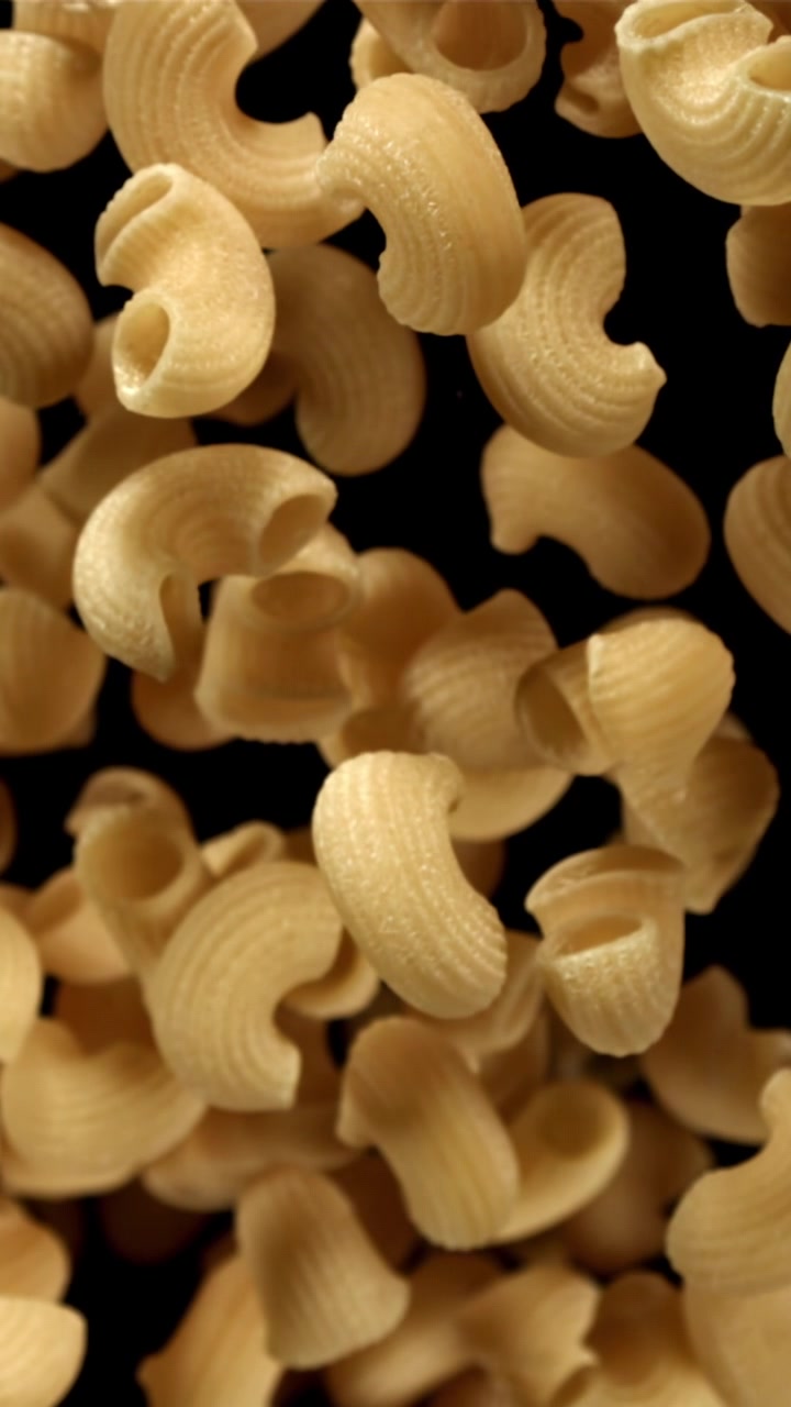Pasta maccheroni secca che cade al rallentatore su sfondo nero.
