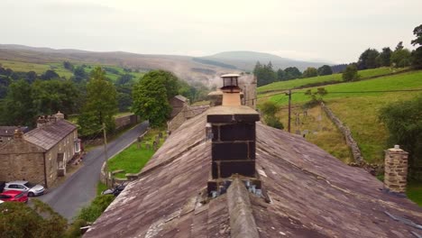 la antena de un dron revela una toma del techo de una antigua cabaña de piedra con humo de chimenea sobre el pueblo de yorkshire