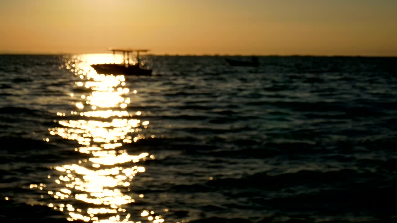 4k 영상, 추상적인 흐릿한 배경, 해가 지거나 해가 뜨는 시간에 작은 파도와 함께 바다 위에 작은 배의 실루, 여름 시간에 열대 해변에서 물 표면과 함께 아름다운 빛 반사