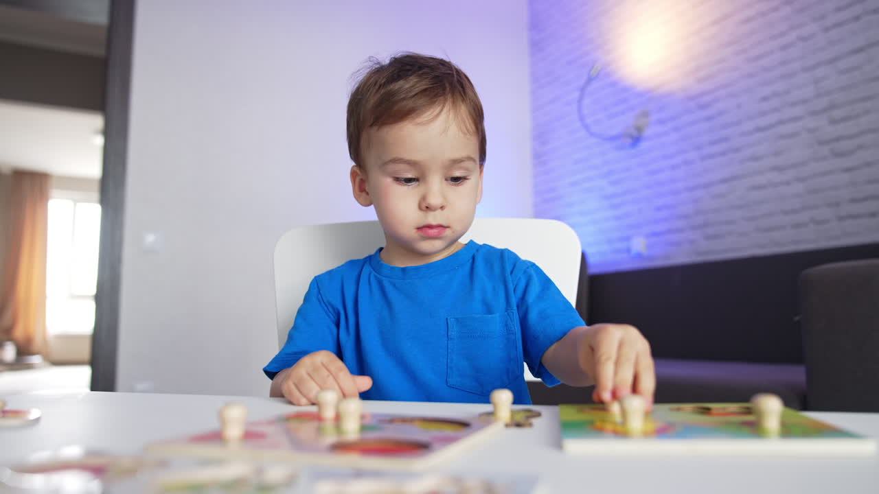 Adorabile bambino dai capelli scuri con una maglietta blu seduto alla scrivania. Un bambino di due anni che compone puzzle tranquillamente.