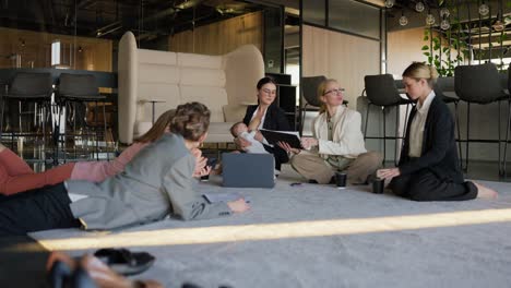 zoom in confident brunette girl in business clothes breastfeeds her little baby during a meeting on the floor on the carpet in a modern office