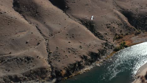 Drohnenaufnahmen,-Die-Einem-Einmotorigen-Hinterlandflugzeug-über-Einen-Fluss-Folgen-Und-Auf-Einer-Abgelegenen-Landebahn-Inmitten-Von-Bergen-In-Der-Wildnis-Des-Frank-Church-River-Of-No-Return-In-Idaho-Landen