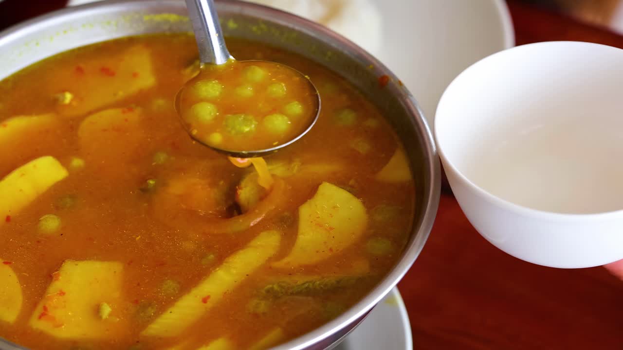 A ladle serves hot vegetable soup from a pot into white bowls, showcasing vibrant ingredients.