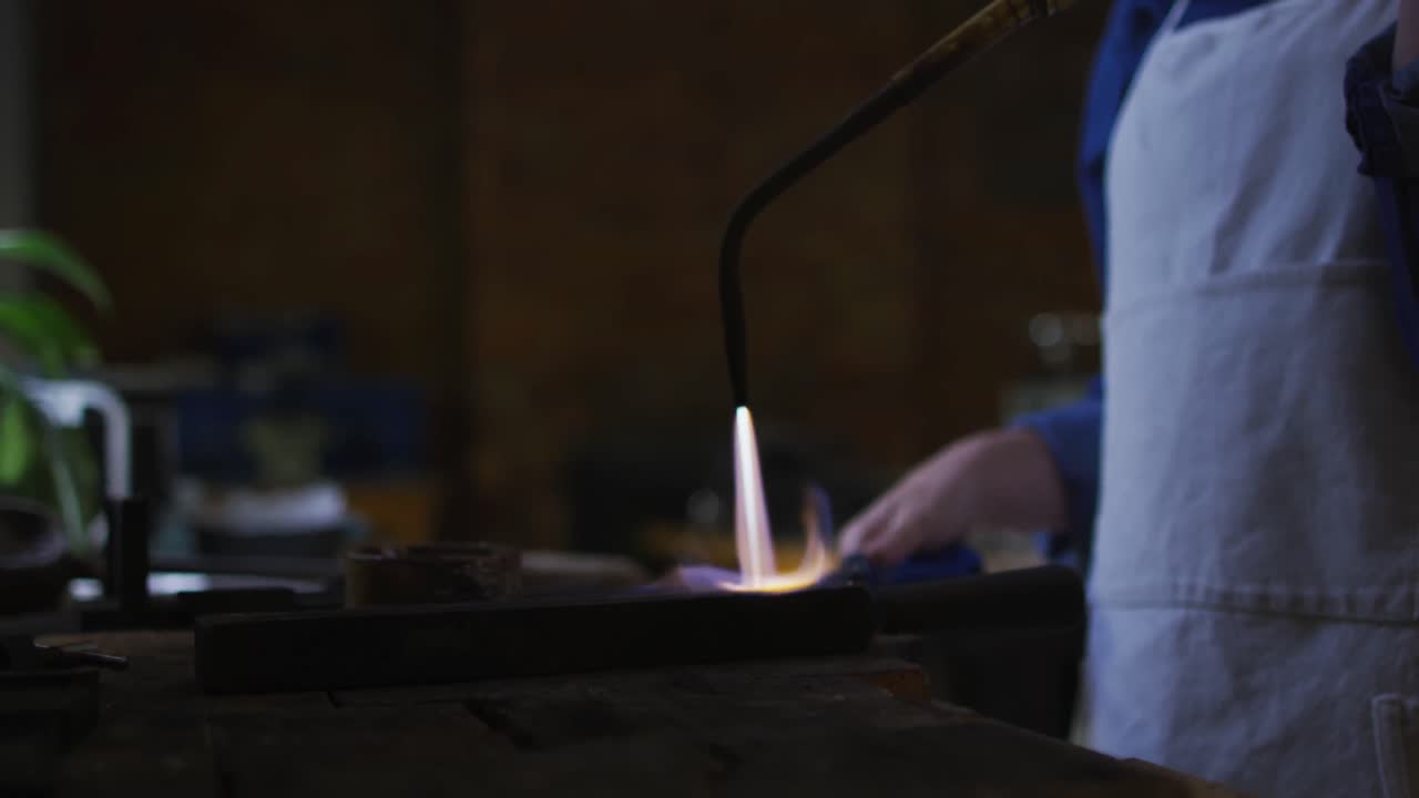 Busto di una gioielliera caucasica in laboratorio, con grembiule, che utilizza un cannello a gas.