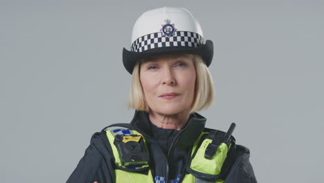 studio portrait of serious mature female police officer against plain background