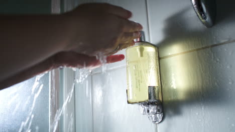 Hands-pushing-a-container-with-soap-under-shower-stream