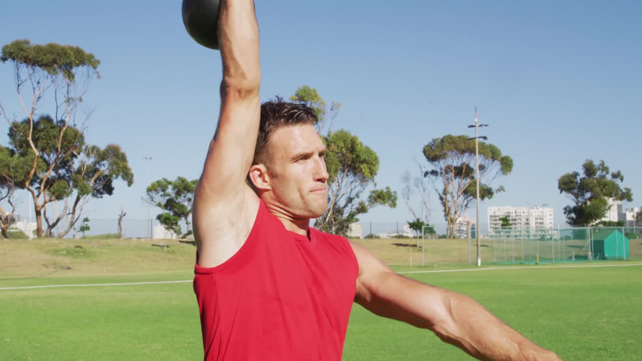 hombre caucásico en forma haciendo ejercicio al aire libre, en cuclillas y levantando pesas de kettlebell con un brazo