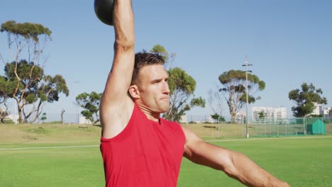 fit caucasian man exercising outdoors, squatting and lifting kettlebell weight with one arm