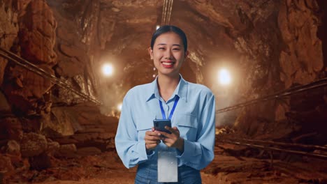 asian female with her smarphone in underground mine tunnel, she is looking at the camera with a smile