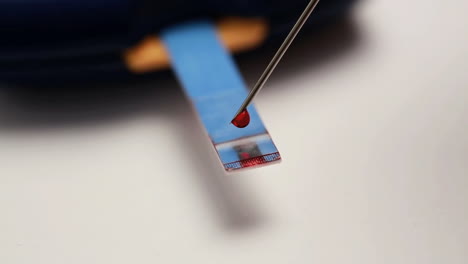 colocación con aguja de una gota de sangre en la tira de ensayo del monitor de glucosa