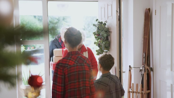 Excited Grandchildren Greeting Grandparents With Presents Visiting On Christmas Day