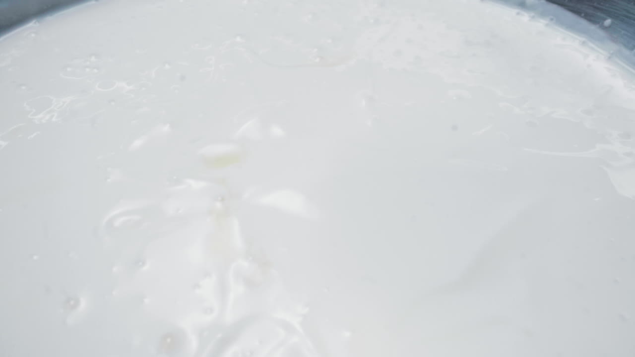 Slow motion close-up shot of mango cubes falling gently into a bowl of smooth white yogurt. The vibrant yellow contrasts with the creamy white texture, creating a visually delicious moment.