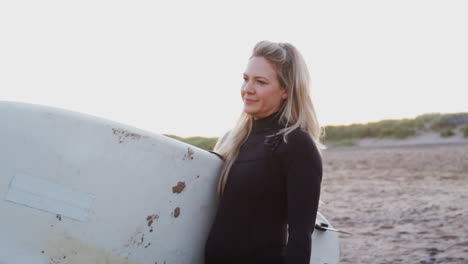 Woman-Wearing-Wetsuit-Walking-Along-Beach-Holding-Surfboard-Enjoying-Surfing-Vacation