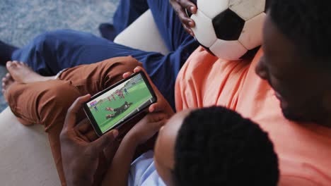 composite of father and son at home watching hockey match on smartphone