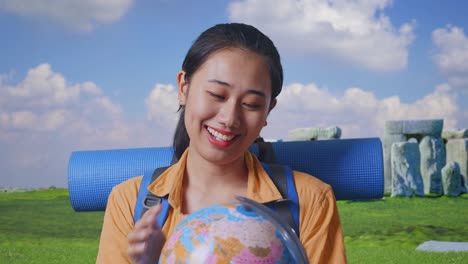 close up of asian female hiker with mountaineering backpack holding world globe in her hands and smiling while traveling in stonehenge