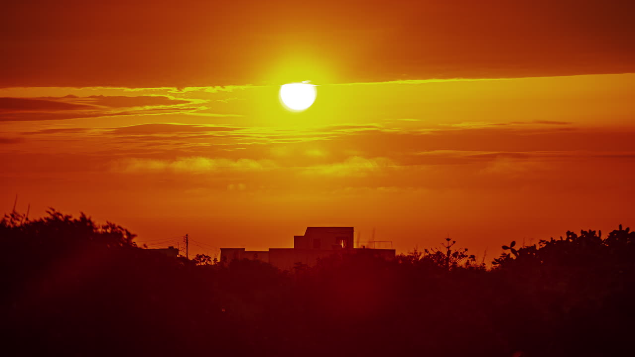 Bright red ball of sun rises like fire above concrete tropical building, timelapse