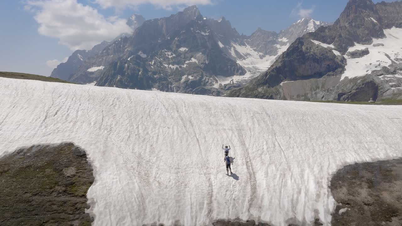 dos excursionistas caminan por senderos de montaña nevados en el mont blanc, rodeados de impresionantes vistas alpinas, el dron se eleva para revelar picos