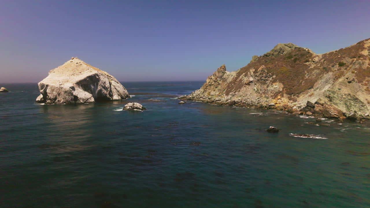 Flying low over the deep blue water of ocean. Approaching the passage between two rocks with algae on the water surface.
