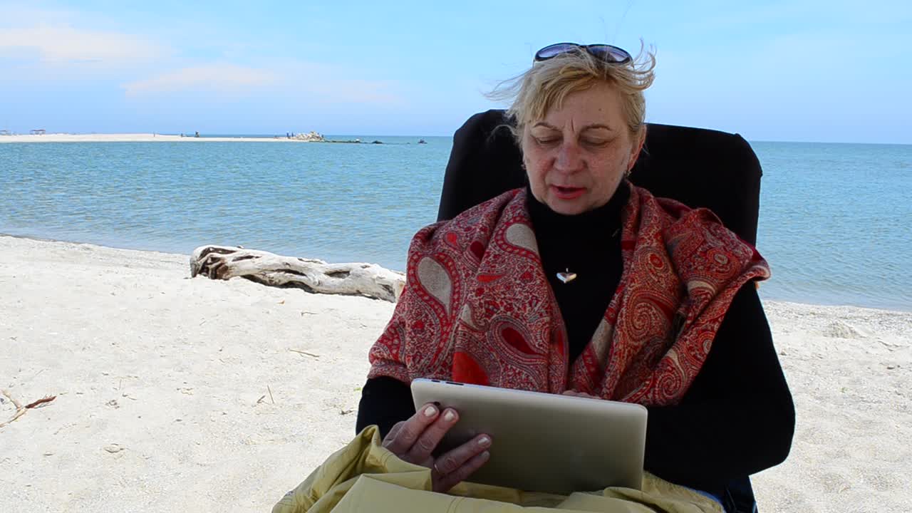 Il tablet nelle mani della signora. Scatto dell'anziana al mare