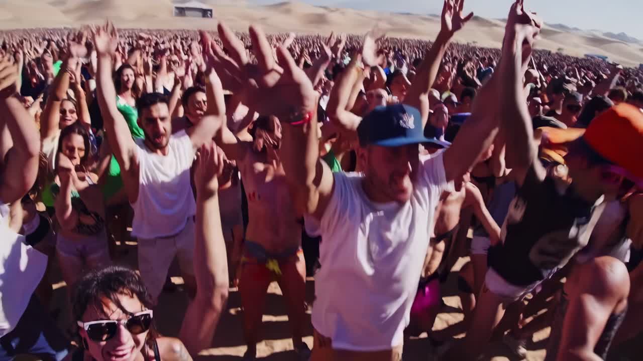 Energetic crowd dancing, arms raised high, immersed in pulsing electronic beats against expansive desert landscape, embodying festival euphoria and collective musical celebration