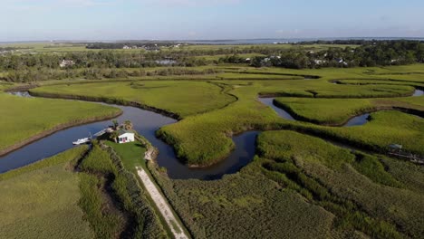 aerial fly over of a small house secluded in the marsh with a small boat in tybee island georgia.