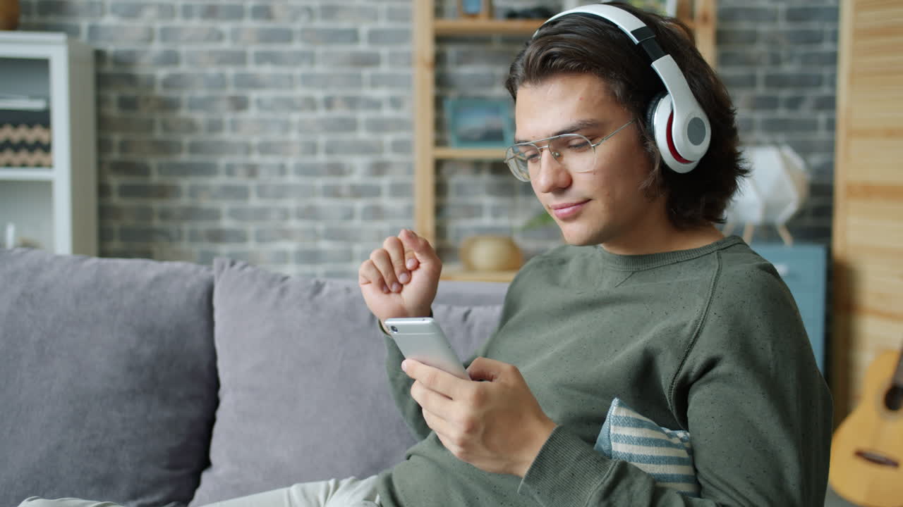 Man Relaxing on Couch, Listening to Music on Smartphone