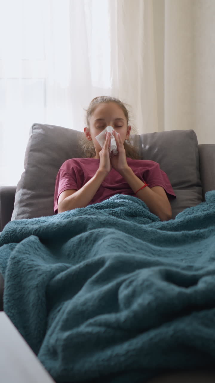 Bambina malata che starnutisce mentre si muove avanti e indietro, fazzoletto in mano, con medicinali sul tavolo, indisposta, bambina stanca coperta da una coperta, che mostra i sintomi dell'influenza a casa