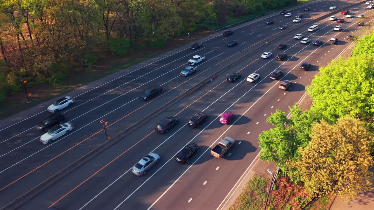 An aerial view along the Southern State Parkway on Long Island, NY, taken during a bright and sunny day. The drone hovers right beside the parkway, looking down from above green treetops.