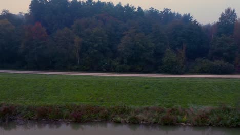 Aerial-view-of-an-empty-path-along-a-grassy-hill-over-a-lake-with-autumn-trees-in-the-background