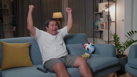 excited asian fat man watches tv in living room