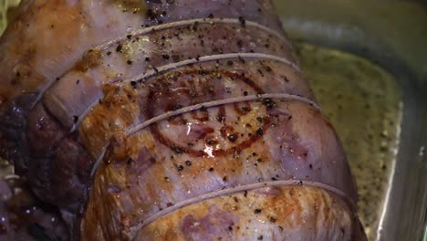 cámara lenta de apuñalar una articulación de cerdo a medio hacer con un cuchillo de cocina serrado en un plato de cocina de vidrio