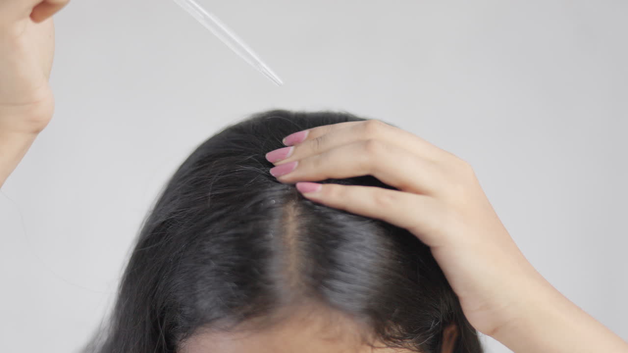 Close up shot of a woman with dropper applying hair serum on scalp in white background, hair care concept