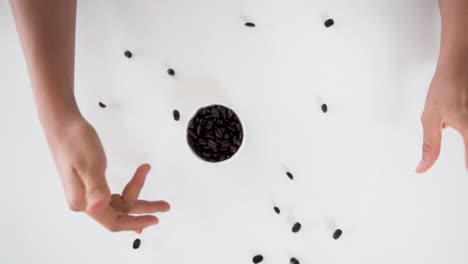 Person's-hands-spin-white-bowl-and-coffee-beans-scatter-around